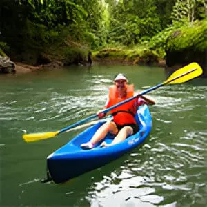 A man in red shirt and orange vest on blue canoe.